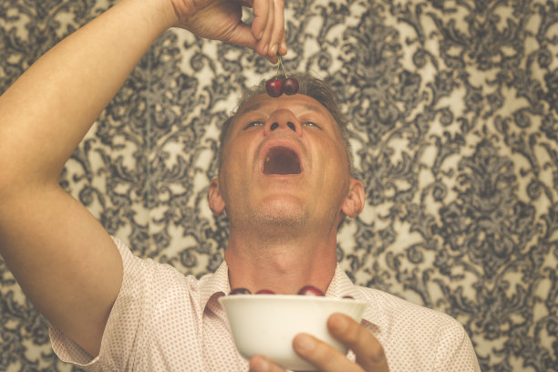 英俊的成年人在他的家里吃着红色，成熟，多汁的樱桃图片下载