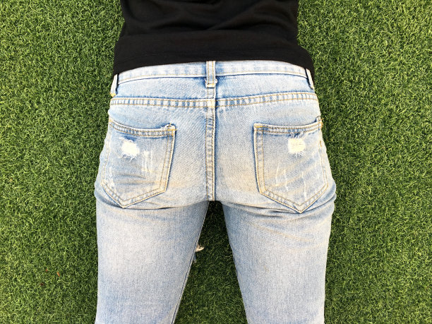 年轻女子底部在紧浅蓝色牛仔裤在绿色草地的背景。图片下载