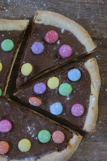 图片自制的巧克力披萨与五彩糖果糖果和糖霜糖，烤披萨皮充满榛子巧克力涂抹儿童，顶部是脆糖涂彩虹smarties巧克力糖果，吃布丁甜点图片下载