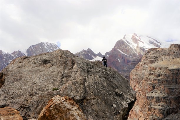 一名男子的剪影爬在岩石上，背景是白雪覆盖的山峰，塔吉克斯坦范山图片下载