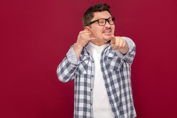 你得给我打电话。肖像英俊的中年商人在休闲格子衬衫，眼镜站与呼叫手势和指向相机。图片下载