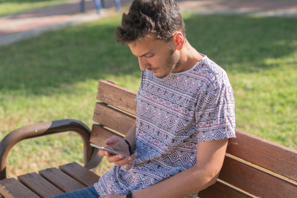 一个在公园长椅上使用智能手机的人图片下载