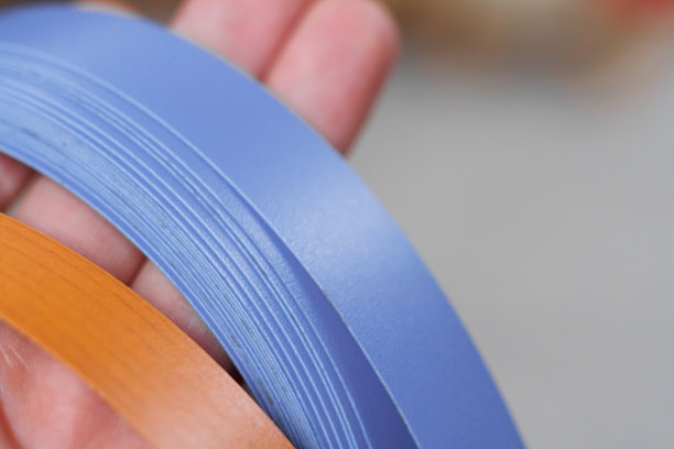 家具配件。一个男人的手握着聚氯乙烯边缘和黑色素制造家具的彩色线轴的特写。谎言金字塔。图片下载