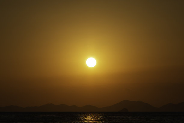 海面上金色的夕阳，背景是山脉。百分之八十的复制空间的图片图片下载