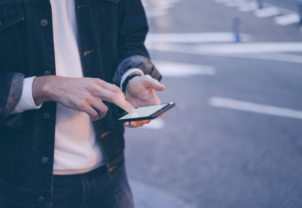 这是一个男性手拿着智能手机的特写照片，晚上在城市街道上搜索互联网或社交网络，嬉皮士在聊天中输入短信图片下载