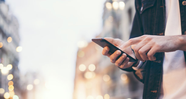 这是一个男性手拿着智能手机的特写照片，晚上在城市街道上搜索互联网或社交网络，嬉皮士在聊天中输入短信图片下载