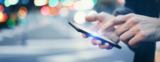 这是一个男性手拿着智能手机的特写照片，晚上在城市街道上搜索互联网或社交网络，嬉皮士在聊天中输入短信图片下载