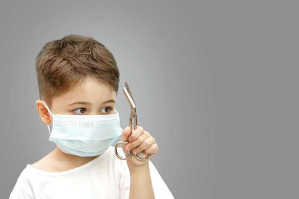 一个带医用面具的白人小男孩在一个孤立的背景下拿着医用剪刀图片下载