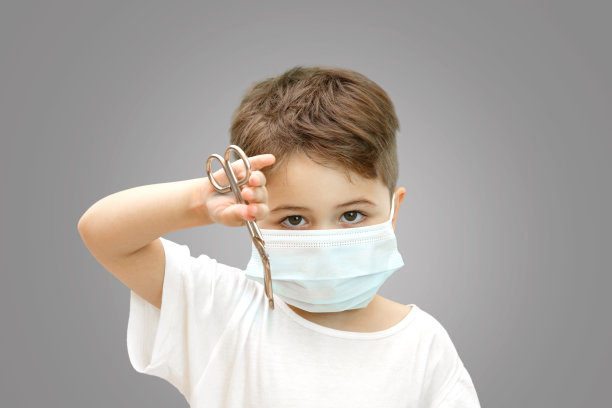 一个带医用面具的白人小男孩在一个孤立的背景下拿着医用剪刀图片下载