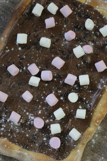 这是自制的巧克力披萨蛋糕，上面点缀着棉花糖、糖屑和糖霜，烤披萨饼皮上覆盖着榛子，上面覆盖着红色和白色的迷你棉花糖热巧克力糖果，为孩子们的生日派对做准备图片下载