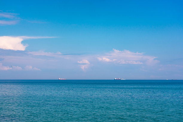 在一个晴朗的日子看黑海。岸上有石头和沙子，地平线上有船。蓝天和美丽的云彩。图片下载