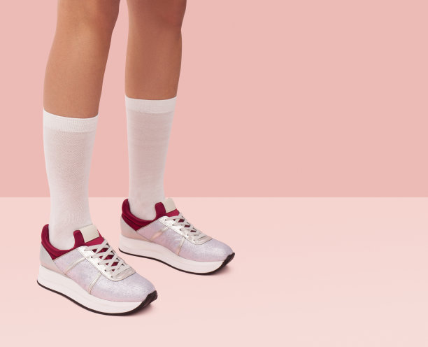穿着白色长筒袜和银色运动鞋的女孩站在珊瑚粉色的背景下图片下载