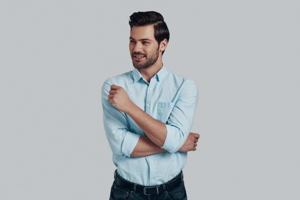 总是充满信心。英俊的年轻人望着别处，面带微笑，站在灰色的背景下图片下载