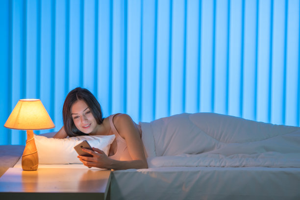 可爱的女人躺在床上打电话。晚上晚上时间图片下载