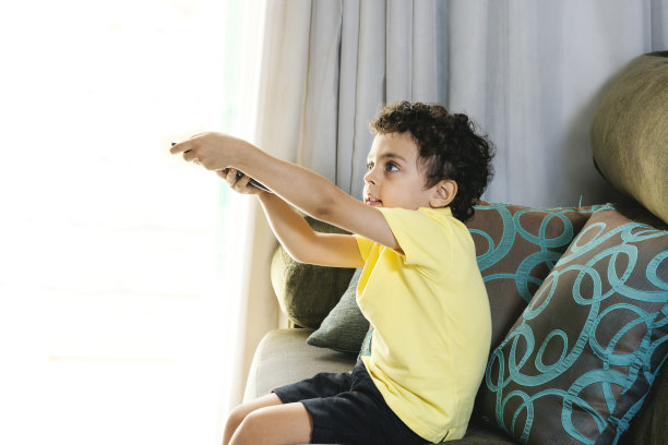 可爱的小男孩坐在沙发上用遥控器看电视图片下载