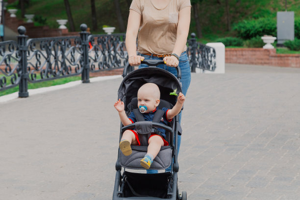 美丽的女人和一个孩子在婴儿车里走过一个夏天的公园图片下载