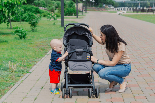 一位年轻的母亲推着婴儿车带着孩子在公园里散步图片下载