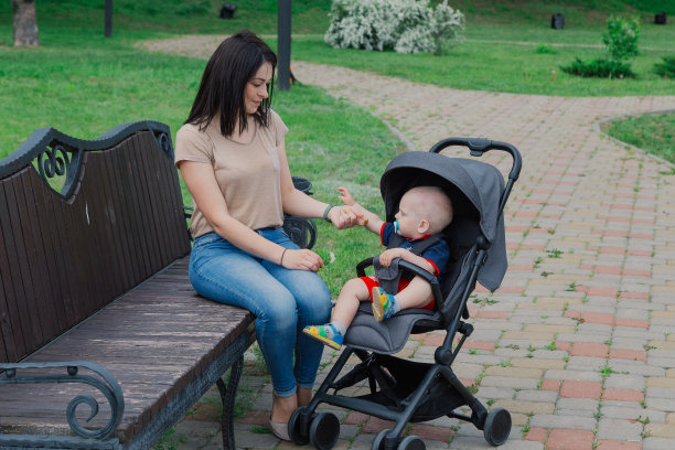 在一个阳光明媚的夏日里，美丽的母亲抱着婴儿车里的婴儿坐在长椅上图片下载