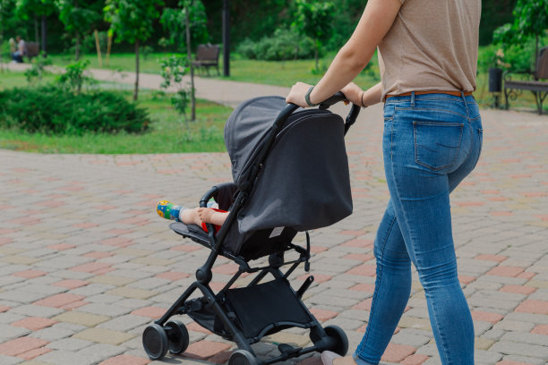 美丽的女人和一个孩子在婴儿车里走过一个夏天的公园图片下载