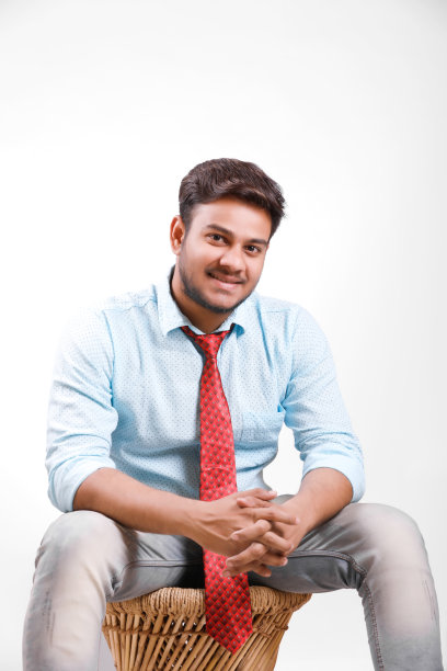 英俊的年轻印度男子坐在桌子上孤立的白色背景图片下载