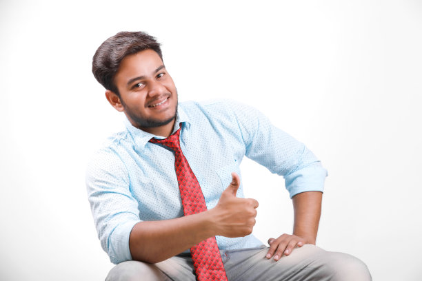 英俊的年轻印度男子坐在桌子上孤立的白色背景图片下载
