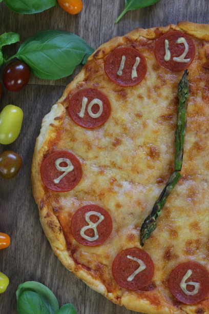这是一个自制披萨时钟的图片，上面有意大利辣香肠片、马苏里拉奶酪和芦笋作为时钟指针，告诉时间19:00 7点，这是意大利披萨餐厅为孩子们的生日聚会食物提供的儿童披萨时钟图片下载