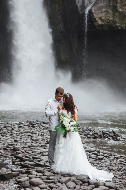年轻的情侣在相爱的新郎和新娘，婚礼的日子附近的山上瀑布。图片下载