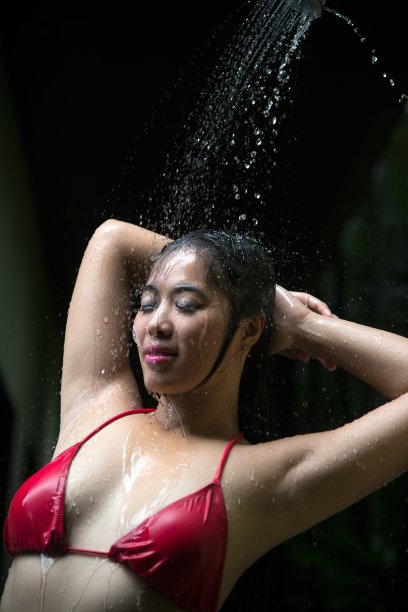 肖像漂亮的亚洲女人穿着红色比基尼摆姿势淋浴洗澡在游泳池和享受。图片下载