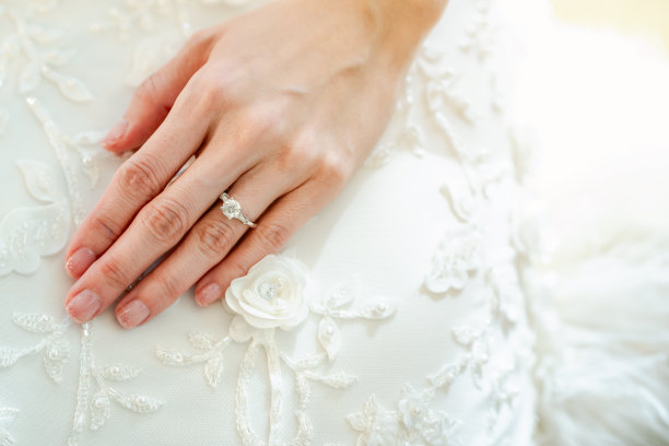 女孩的左手无名指上戴着一枚戒指。把你的手放在白色的婚纱上。图片下载
