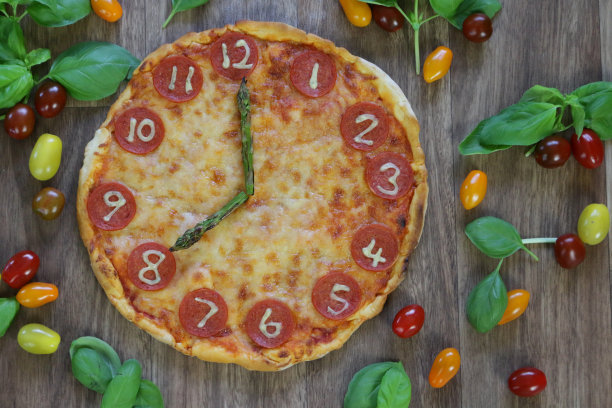 这是一个自制披萨时钟的图片，上面有意大利辣香肠片、马苏里拉奶酪和芦笋作为时钟指针，显示时间08:00，这是意大利披萨餐厅为孩子们的生日聚会食物准备的儿童披萨时钟图片下载