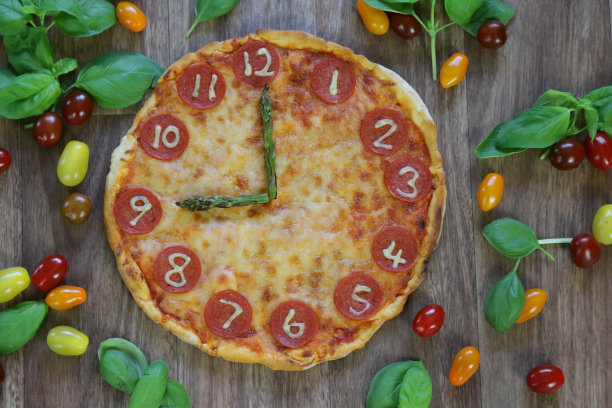 这是一个自制披萨时钟的图片，上面有意大利辣香肠片、马苏里拉奶酪和芦笋作为时钟指针，显示时间09:00 9:00，这是意大利披萨餐厅为孩子们的生日派对提供的儿童披萨时钟图片下载