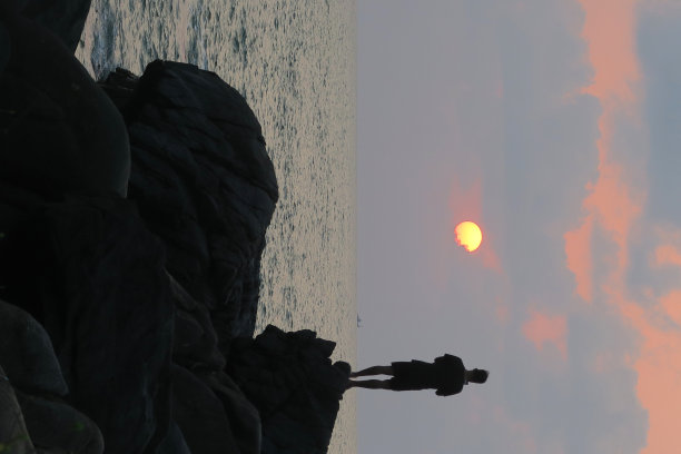 印度游客在度假站在岩石上自拍照片在海滩橙色日落拿着手机相机，剪影自拍男子度假果阿海滩自拍手机太阳，太阳镜，沙子，海边的倒影图片下载