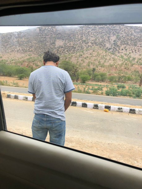 印度男子在路边高速公路上小便，在印度德里附近的出租车旁小便，穿着蓝色牛仔牛仔裤和t恤的男子急需厕所小便器小便图片下载