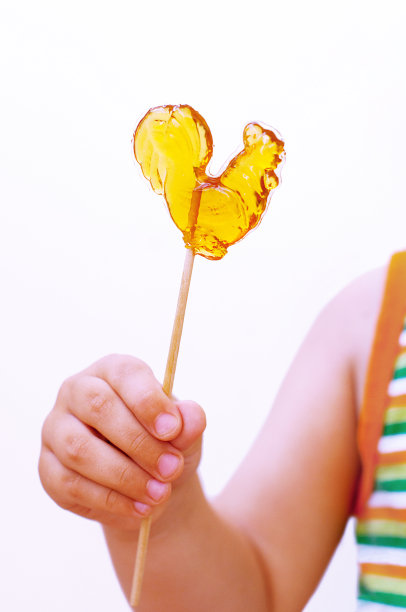 婴儿手里拿着小公鸡形状的棒棒糖。图片下载