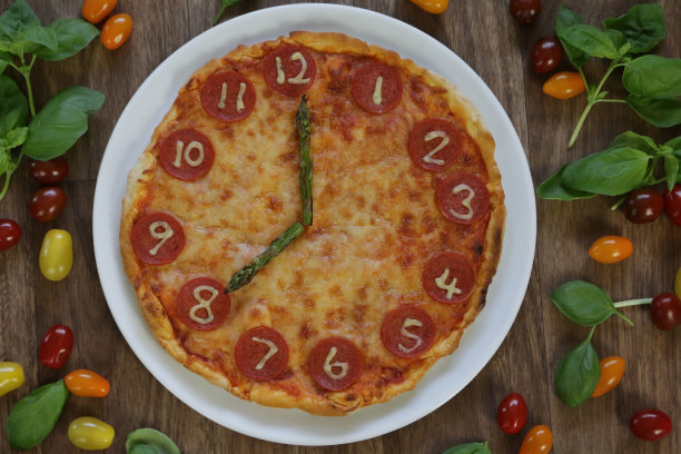 这是一个自制披萨时钟的图片，上面有意大利辣香肠片、马苏里拉奶酪和芦笋作为时钟指针，显示时间08:00，这是意大利披萨餐厅为孩子们的生日聚会食物准备的儿童披萨时钟图片下载