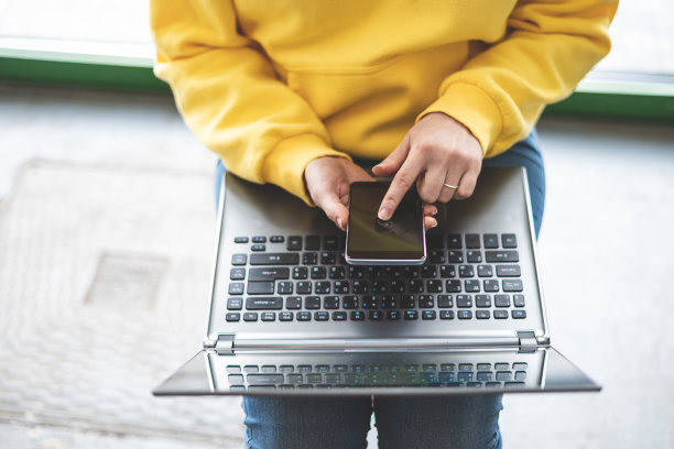 高角度以上俯视图裁剪照片的女士人在趋势流行的衣服。她坐在时尚风格的咖啡店里，用手提电脑和便携式电话设备把手指放在触摸屏上图片下载