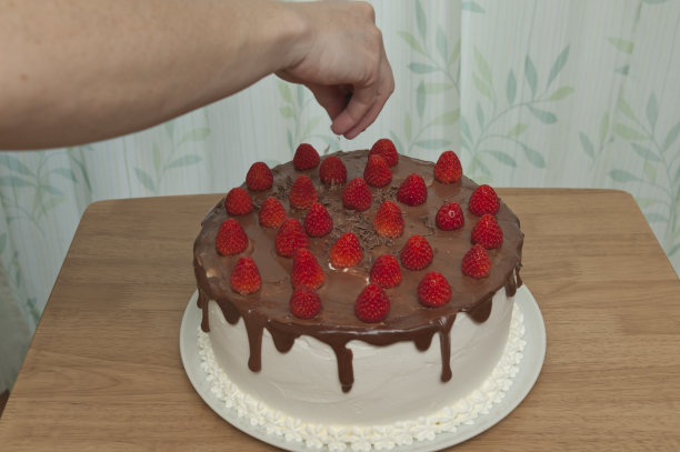 一名女子将磨碎的巧克力撒在蛋糕上，再撒上巧克力糖浆和草莓。图片下载