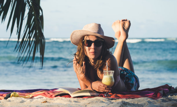 戴着帽子和太阳镜的漂亮女人在沙滩上放松。图片下载