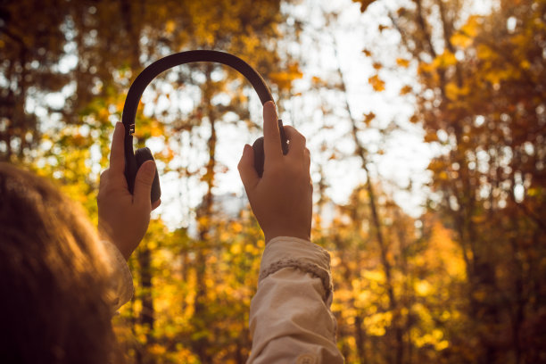 女性戴着耳机在公园里散步，听着秋天森林里的声音或音乐。的概念。印度夏季图片下载