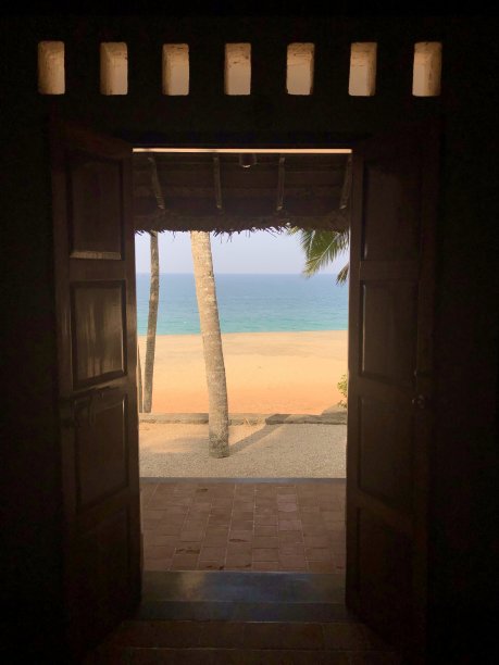 在印度南部喀拉拉邦/果阿邦的户外，通过开着面板的双扇门/木制百叶窗可以看到热带海滩的景象，海滨度假开放的前门，金色的阳光，大海，沙子，椰子树和砾石露台图片下载