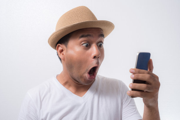 年轻的亚洲男子看起来智能手机和感到震惊和惊讶过度的面部表情。图片下载