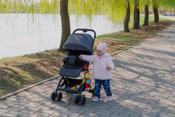 一个小女孩在公园里推着婴儿车。孩子在公园里玩婴儿车图片下载