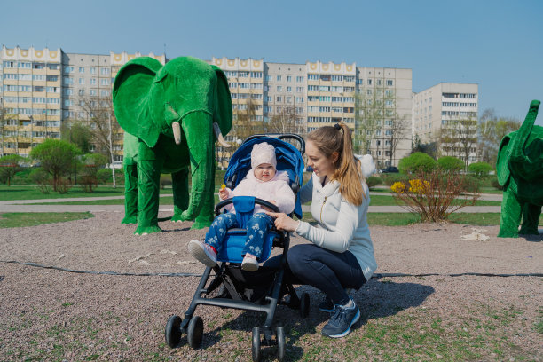 美丽的年轻母亲抱着婴儿车在城市公园里图片下载