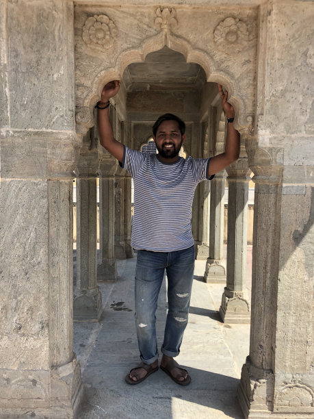 年轻英俊的印度男子在印度观光旅游手举过头顶，在有柱子的寺庙的石拱上休息，亚洲印度教印度男子与破洞牛仔t恤摆姿势，在德里阴凉炎热的天气休息图片下载