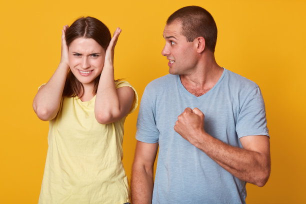 照片中危险的男人握紧拳头，准备为女友制造痛苦，看着她不满的神情，紧张的黑发女子用手捂着头，神情焦虑。争吵的概念。图片下载