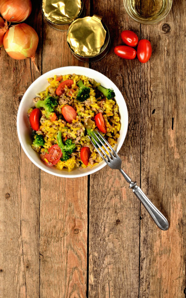 从上面看，碗里有金枪鱼烩饭和蔬菜，西红柿，花椰菜和欧芹，洋葱，罐头和油在背景-垂直照片图片下载