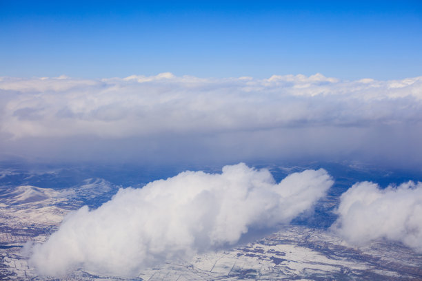 白雪皑皑的山峰上，白云悬在蓝天上。从飞机窗户拍摄的航拍照片。图片下载
