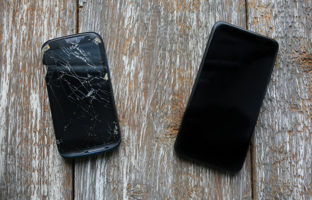 坠毁的黑色智能手机躺在新手机附近的木制背景上。液晶触摸屏破碎。信息技术的照片。新老。图片下载