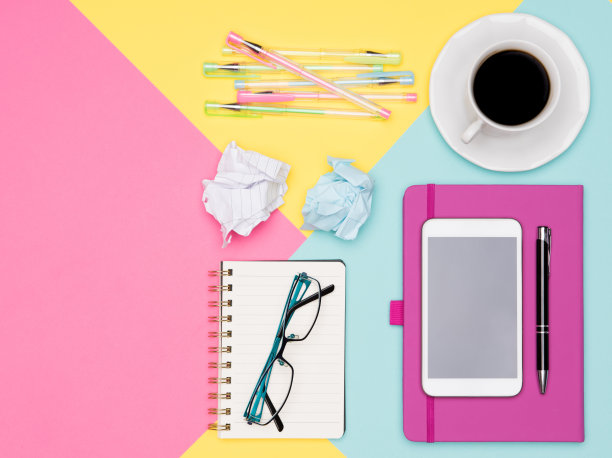 办公室办公桌工作空间平整。俯视图照片的工作空间与智能手机，咖啡杯和打开记事本在柔和的背景。彩色办公桌。图片下载