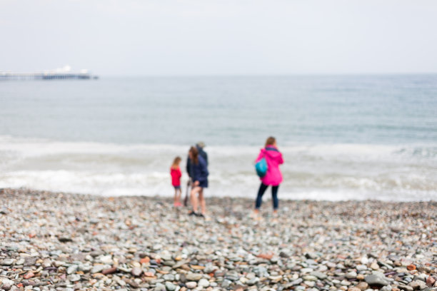 模糊的照片，人们站在岩石沙滩上，背景是大海和天空。孩子们在海边散步。人与自然的抽象模糊照片。图片下载